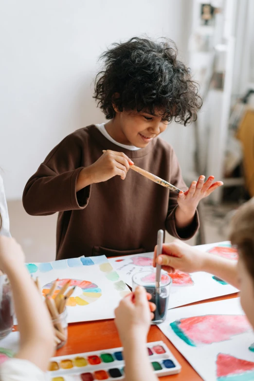 a group of children sitting at a table painting, pexels contest winner, process art, holding a paintbrush in his hand, painting on a badge, wholesome, trending on