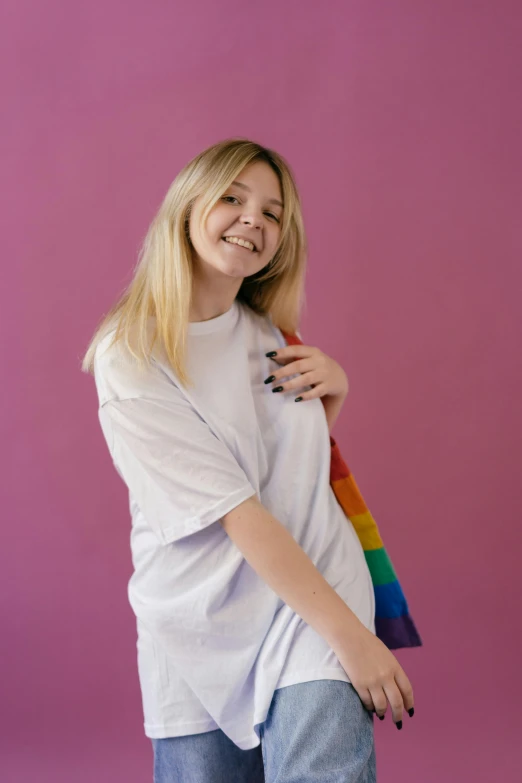 a woman standing in front of a pink background, dressed in a white t shirt, rainbow clothes, sydney sweeney, profile image