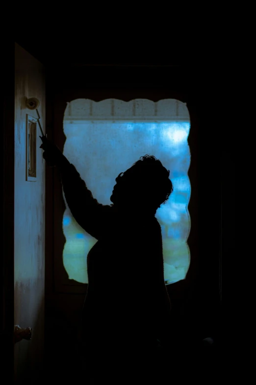 a silhouette of a person standing in front of a window, inspired by Gregory Crewdson, pexels contest winner, hand on the doorknob, no light reflecting off paint, raking light, cold blue light