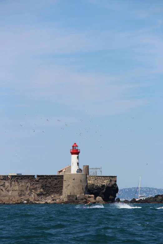 a lighthouse in the middle of a body of water, cannes, with lots of dark grey rocks, square, telephoto
