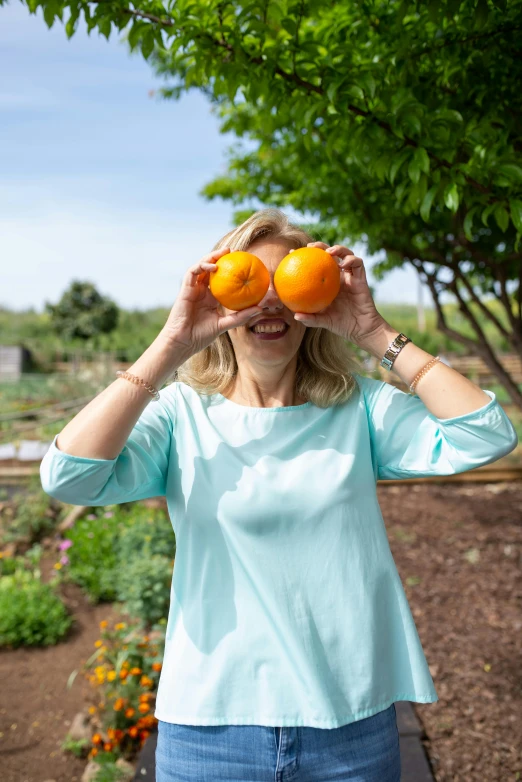 a woman holding two oranges in front of her eyes, by Ellen Gallagher, pexels contest winner, garden behind the glasses, smiling playfully, blue and orange color scheme, avatar image