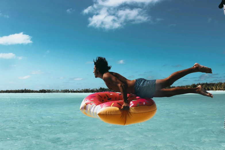 a man flying through the air over a body of water, by Nina Hamnett, pexels contest winner, polynesian style, donut, tan skin, inflatable