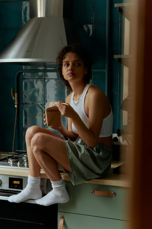 a woman sitting on top of a stove in a kitchen, inspired by Nan Goldin, trending on pexels, bra and shorts streetwear, nathalie emmanuel, people inside eating meals, dafne keen