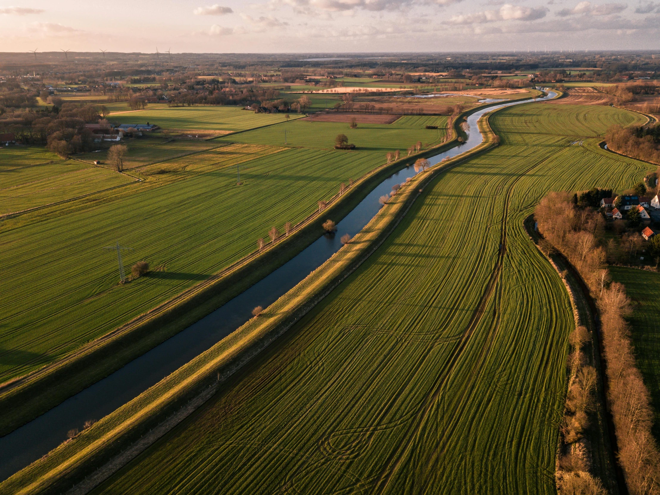 a river running through a lush green field, by Eglon van der Neer, pexels contest winner, renaissance, canals, winter sun, wide high angle view, golden hour light