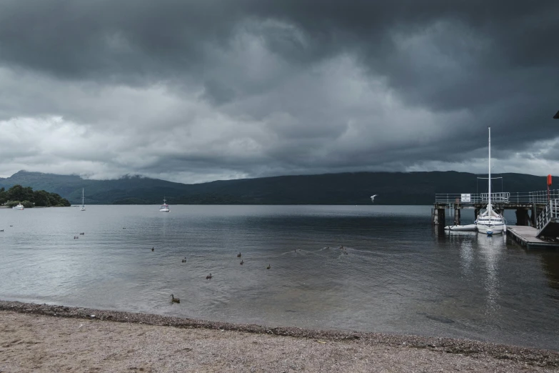 a beach next to a body of water under a cloudy sky, a portrait, inspired by Thomas Struth, unsplash, hurufiyya, loch ness monster, docks, dark grey, grey