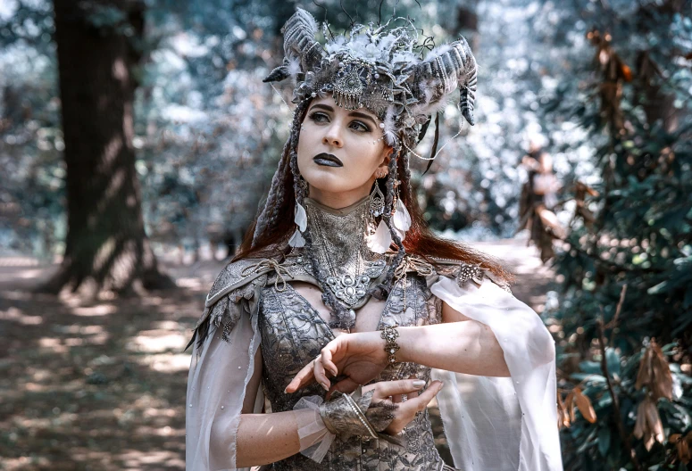 a woman dressed in silver standing in a forest, inspired by Apollinary Vasnetsov, pexels contest winner, fantasy art, wearing gothic accessories, with horns, elaborate costume, grey