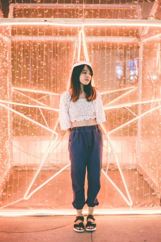 a woman standing in front of a building with christmas lights, by Tan Ting-pho, pexels contest winner, light and space, kawaii shirt and jeans, geometric backdrop; led, in white room, wearing a cropped top