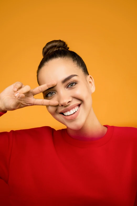 a woman in a red shirt making a frame with her hands, trending on pexels, pop art, perfect smile vogue, angular eyebrows, topknot, orange hue