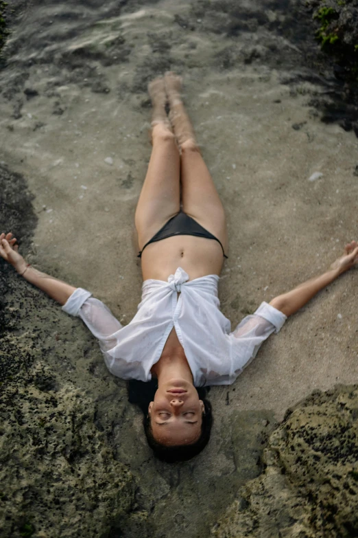 a woman laying on top of a sandy beach, inspired by Ren Hang, unsplash, renaissance, bali, anatomy, standing on rocky ground, high angle