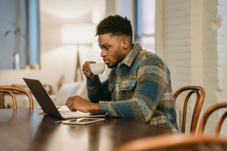 a man sitting at a table with a laptop and a cup of coffee, by Carey Morris, pexels contest winner, jaylen brown, performing, avatar image, concentration