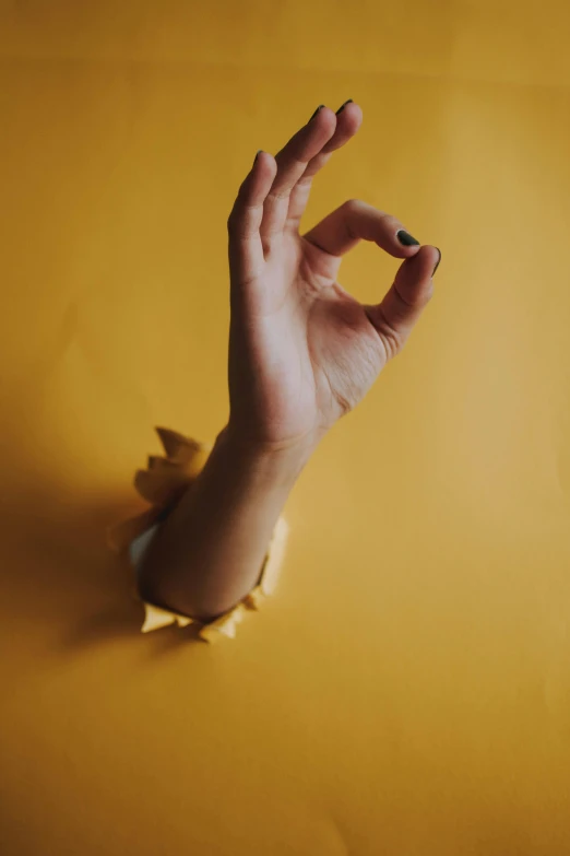 a hand reaching out of a hole in a wall, trending on pexels, yellow backdrop, anjali mudra, mangled, single body