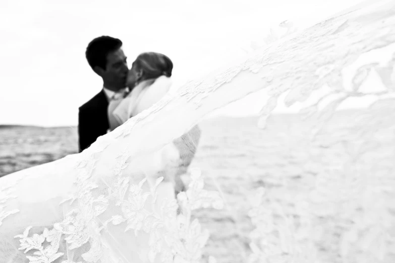 a bride and groom kissing on the beach, a black and white photo, by Caroline Mytinger, romanticism, decoration, white lace, elevation, version 3