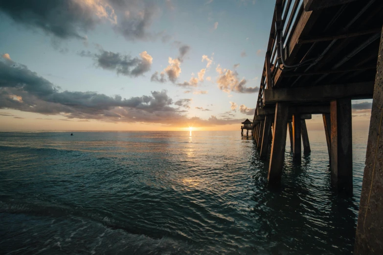 a pier stretches out into the ocean at sunset, by Niko Henrichon, daylight, sunset beach, multiple stories, conde nast traveler photo