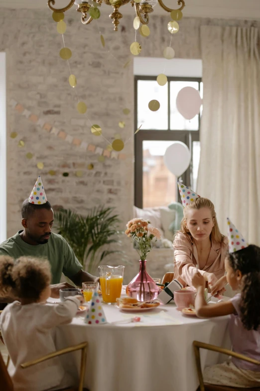 a group of people sitting around a table at a party, with a kid, profile image, cinematic image, thumbnail