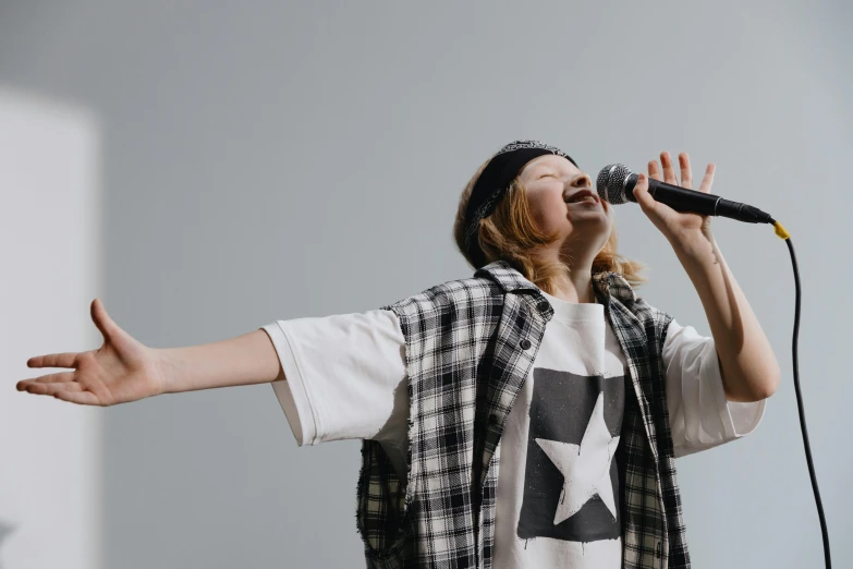 a woman singing into a microphone on a stage, trending on pexels, antipodeans, wearing a tee shirt and combats, little kid, on a gray background, gigachad jesus