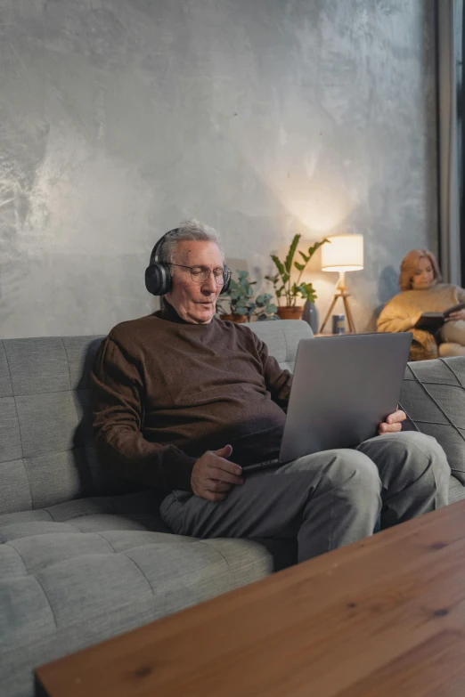 a man sitting on a couch with a laptop, wearing a headset, an oldman, dark grey haired man, casually dressed