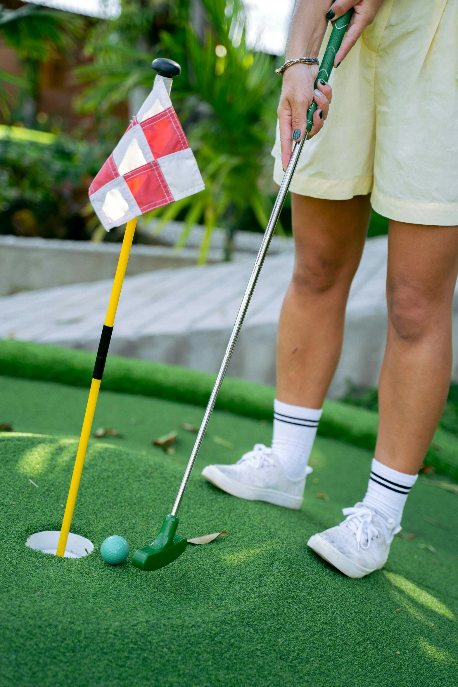 a woman putting a golf ball into a hole, wearing golf shorts, singapore, square, multicoloured