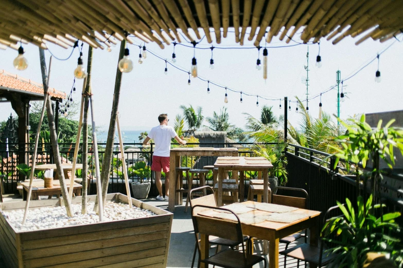 a man standing on top of a roof next to a wooden table, tropical vibe, bao phan, oceanside, patio