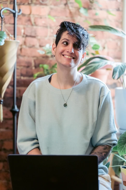 a woman sitting in front of a laptop computer, a portrait, inspired by Anita Malfatti, next to a plant, smiling and looking directly, tattooed, pictured from the shoulders up