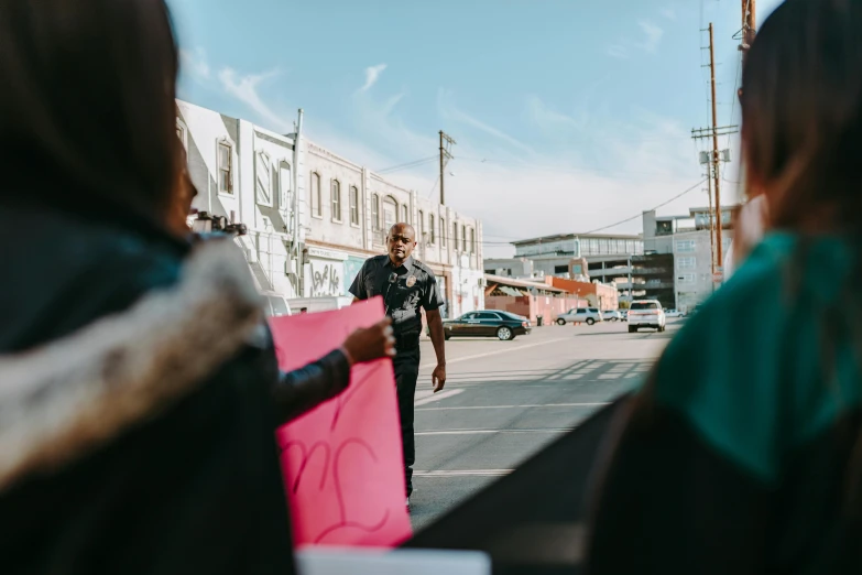 a man standing next to a woman holding a pink sign, by Lee Loughridge, pexels contest winner, happening, police officers, view from the streets, alexis franklin, essence