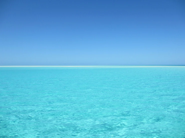 a large body of water in the middle of the ocean, light blue sky, bright vivid colours, crystal waters