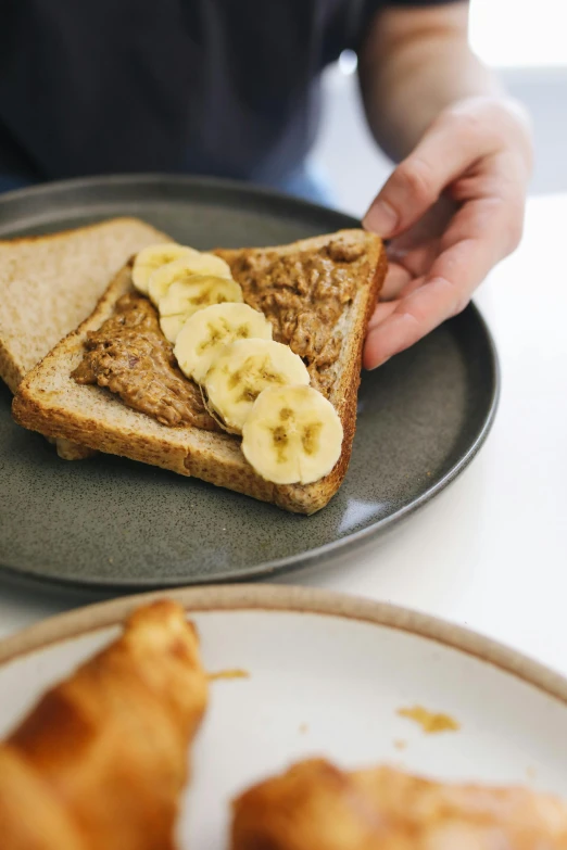 a person sitting at a table with a plate of food, inspired by Richmond Barthé, unsplash, toast, banana, brood spreading, frontal shot