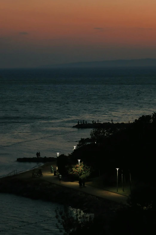 a lighthouse sitting on top of a beach next to the ocean, people at night, kamakura scenery, ((sunset)), low iso