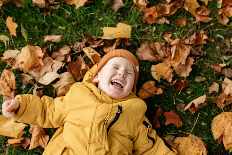 a small child laying on top of a pile of leaves, pexels contest winner, laughing and joking, yellow clothes, 1 5 6 6, brown