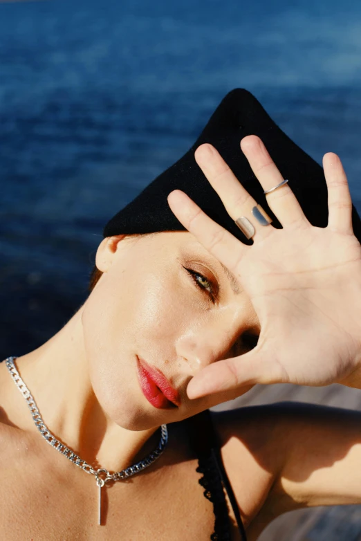 a woman posing in front of a body of water, an album cover, inspired by Tamara Lempicka, trending on pexels, photo of a hand jewellery model, breton cap, pale skin, chaumet