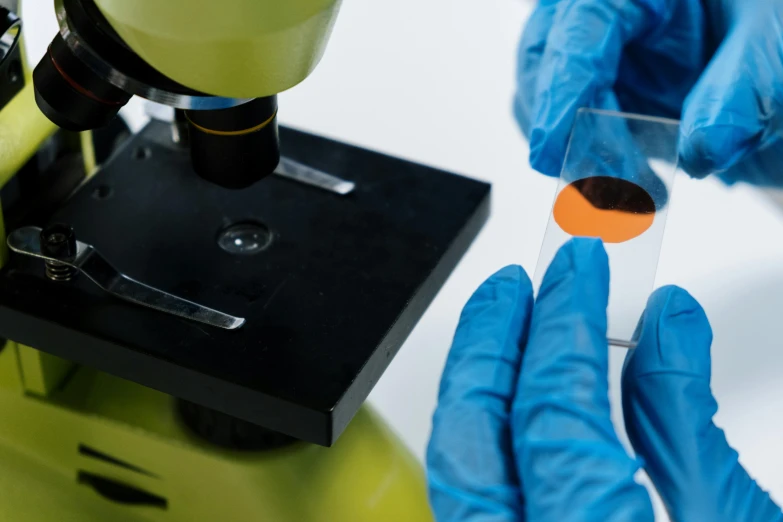 a person in blue gloves is using a microscope, orange, modular graphene, detailed product image, middle shot