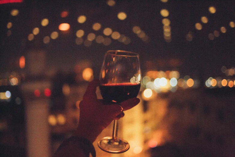 a person holding a glass of wine in their hand, pexels contest winner, city lights in the background, 💋 💄 👠 👗, grainy, sydney hanson