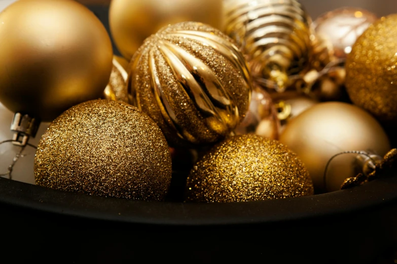 a bowl filled with gold ornaments on top of a table, by Adam Marczyński, shutterstock, up close shot, organic ornaments, full colour, dark tone