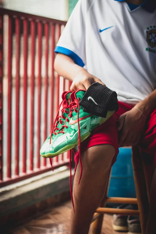 a man sitting on a chair holding a pair of shoes, pexels contest winner, green and red, neymar, nike, tournament