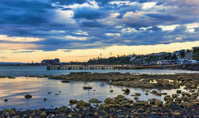 a body of water surrounded by rocks under a cloudy sky, harbour, golden hour photograph, wood pier and houses, “ iron bark