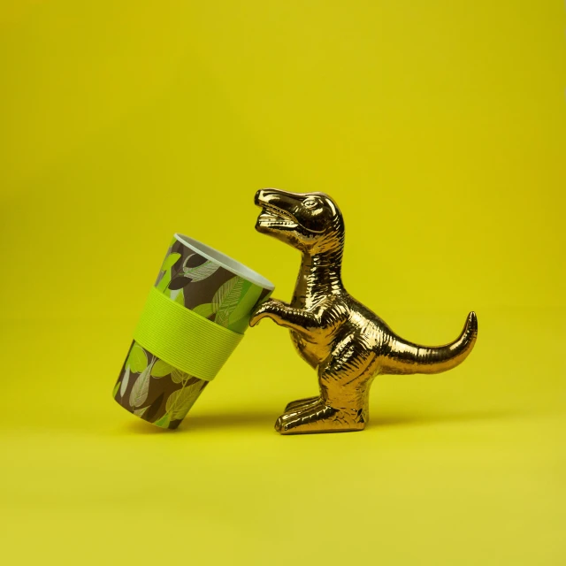 a toy dinosaur holding a cup on a yellow background, inspired by Sarah Lucas, unsplash, graffiti, golden and copper shining armor, camouflage, official product image, brass plated