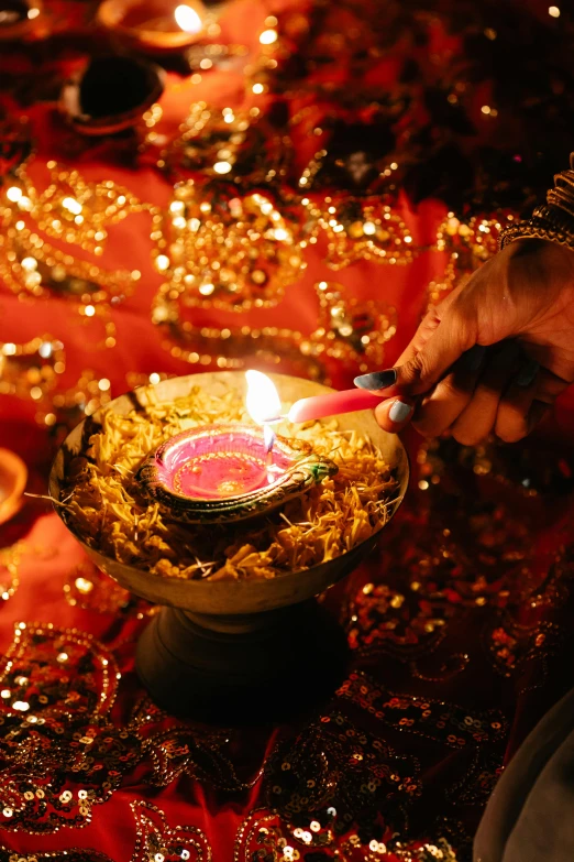 a close up of a person lighting a candle, hurufiyya, red and gold sumptuous garb, hindu, led, vibrant setting