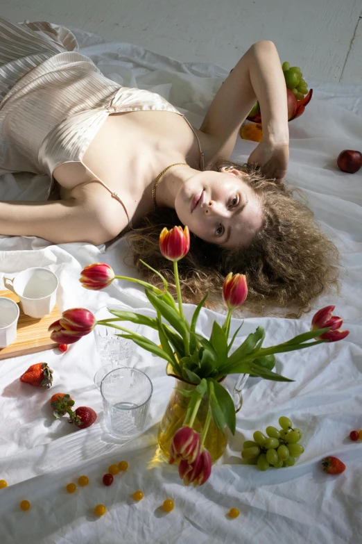 a woman laying on a bed with fruit and flowers, pexels contest winner, renaissance, tulips, white tablecloth, sultry, picnic