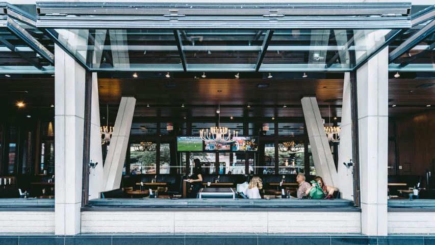 a group of people sitting at a table in a restaurant, by Meredith Dillman, unsplash, bars on the windows, exterior view, wings open, paler. millions of glass-walled