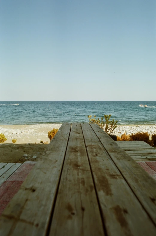 a wooden table sitting on top of a sandy beach, by Tamas Galambos, scanned, backyard, black sea, low ultrawide shot