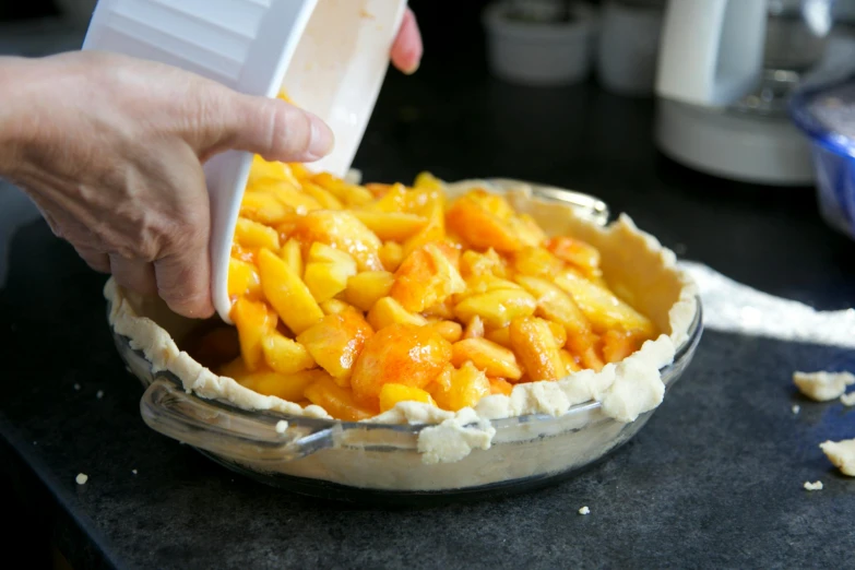 a person putting something in a pie crust, a pastel, mango, filling with water, peach, frontal shot