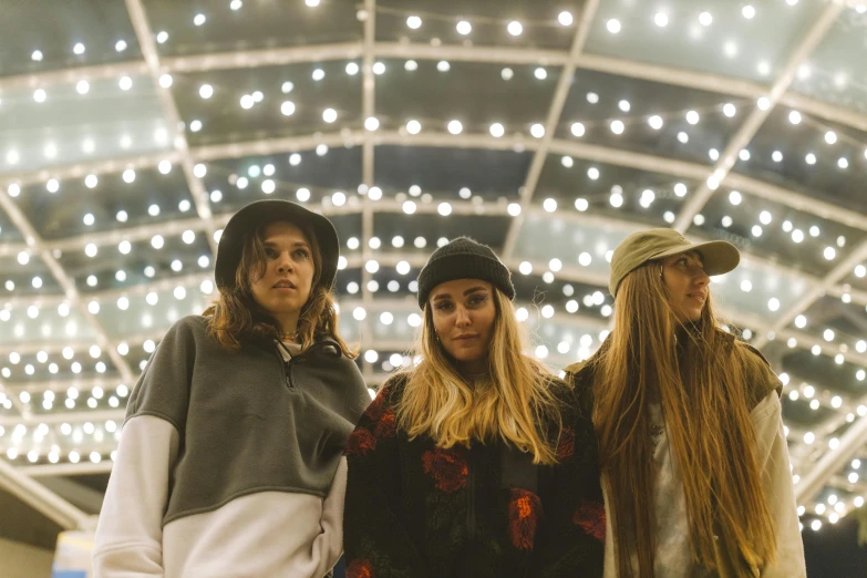 a group of three women standing next to each other, unsplash, antipodeans, wearing beanie, lights inside, blonde, biodome