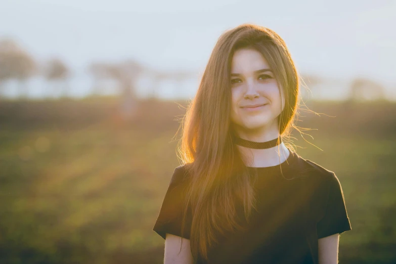 a woman with long hair standing in a field, pexels contest winner, wearing a black shirt, 18 years old, warm glow, avatar image