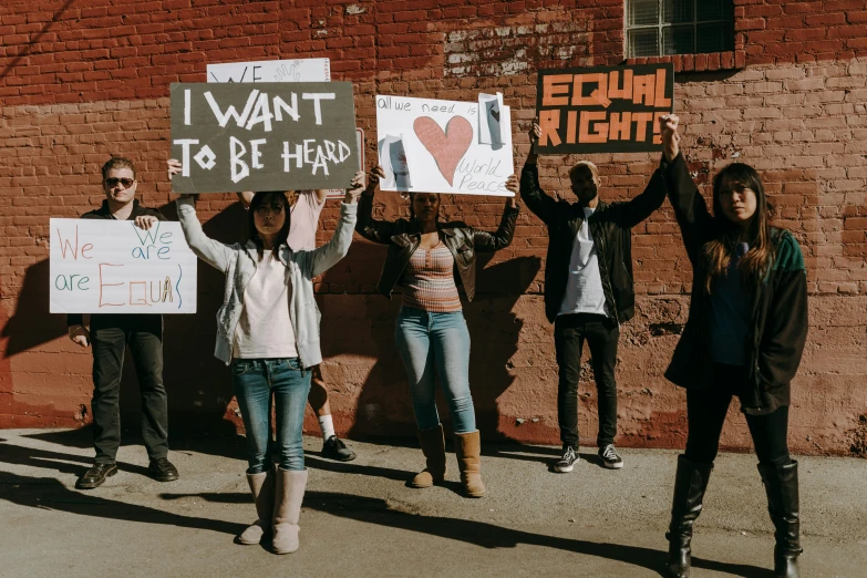 a group of people holding up signs in front of a brick wall, a photo, by Julia Pishtar, trending on pexels, black arts movement, background image, gay rights, a person standing in front of a, 3 4 5 3 1