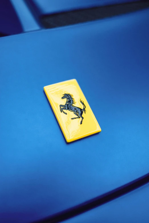 a ferrari badge on the hood of a blue car, inspired by Bernardo Cavallino, synthetism, on yellow paper, 2 0 1 9, enamel, high detail iconic character