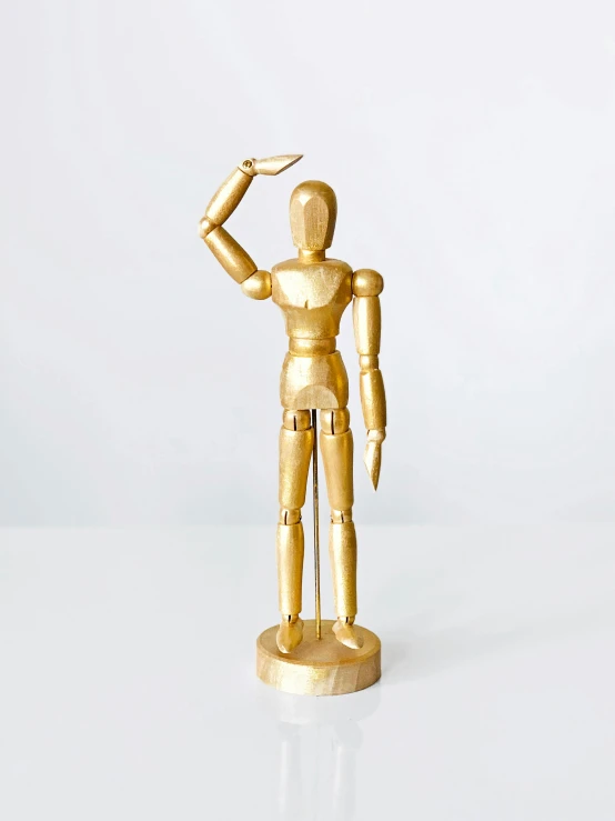 a gold figurine stands on a white surface, by Gavin Hamilton, wood art, oscar winning, back arched, robotic left arm