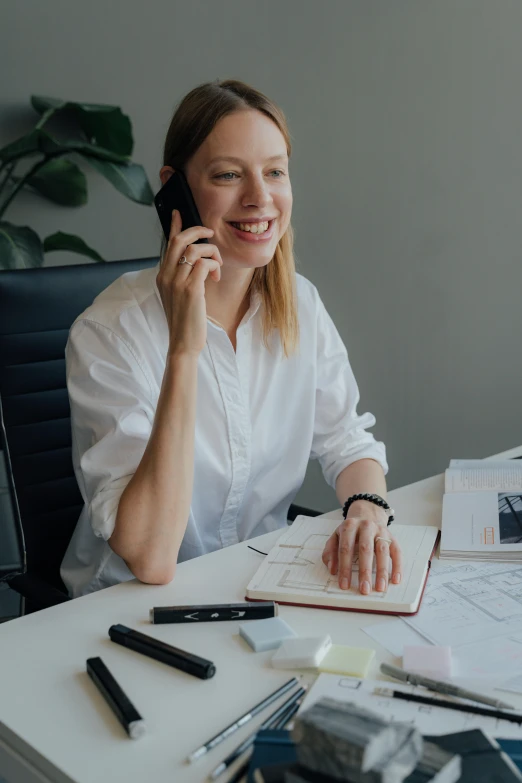 a woman sitting at a desk talking on a cell phone, ux, very consistent, smiling slightly, scandinavian design