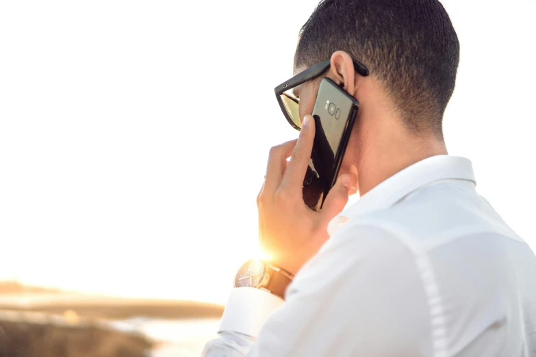 a man in a white shirt talking on a cell phone, by Niko Henrichon, trending on pexels, renaissance, blocking the sun, man with glasses, corporate phone app icon, looking into the horizon