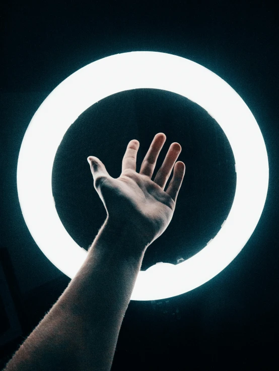 a person holding their hand up in front of a circular light, instagram post, on a black background, ring light, from below