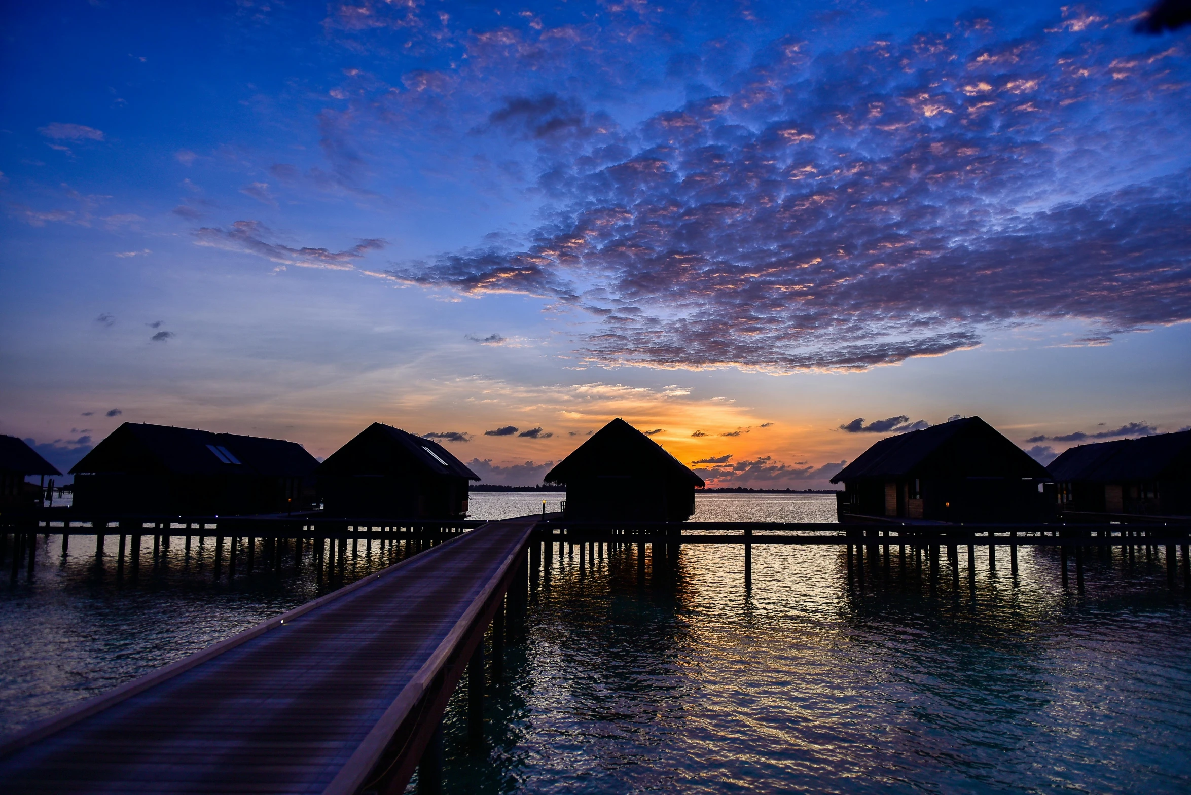 a dock in the middle of a body of water, hurufiyya, in the sunset, huts, profile image, conde nast traveler photo