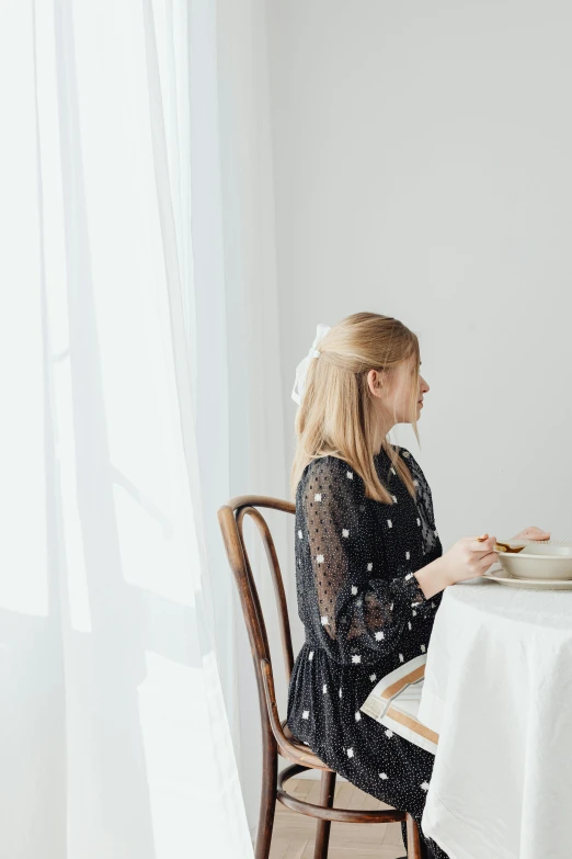 a woman sitting at a table reading a book, inspired by Modest Urgell, dreamy style, polka dot, fine dining, in a white room